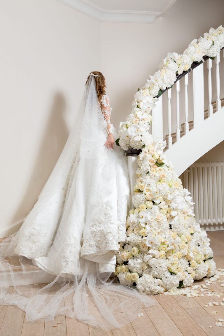 Braut laeuft im Hochzeitskleid die Treppe hoch mit weisser Blumendekoration 768x1152